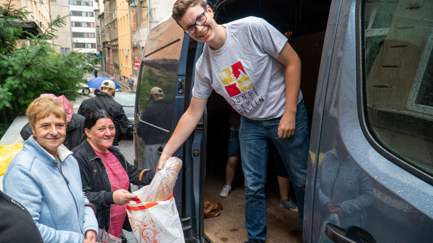 Armenküche, junge Mann steht in einem Kleinbus und gibt zwei Frauen einen Laib Brot, Balkan, Junge Leute Helfen, Arme, Hilfe, Not